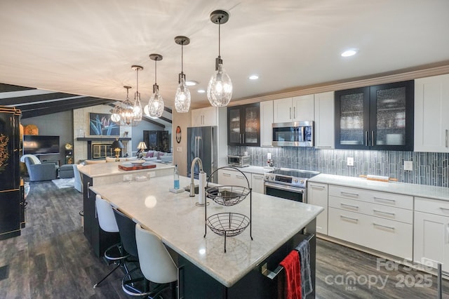 7945 Placid Ct, Denver, NC 28037 - kitchen featuring appliances with stainless steel finishes, dark wood-style floors, tasteful backsplash, a kitchen island with sink, and a kitchen breakfast bar