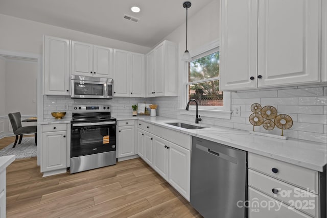 7213 Baniff Cir, Charlotte, NC 28277 - kitchen featuring stainless steel appliances, white cabinets, light stone countertops, light wood finished floors, and pendant lighting