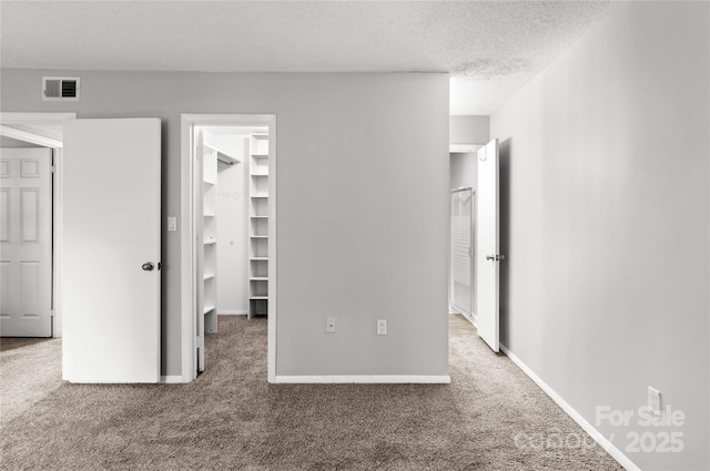 2205 Sunderland Rd Unit 129D, Winston Salem, NC 27103 - unfurnished bedroom with carpet floors, a walk in closet, a textured ceiling, a closet, and baseboards