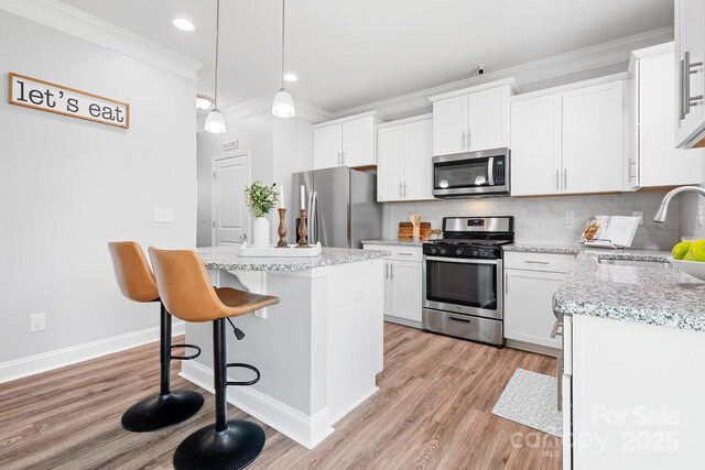 3038 Burnello Ct, Iron Station, NC 28080 - kitchen featuring appliances with stainless steel finishes, crown molding, a kitchen island, light wood-style flooring, and decorative backsplash