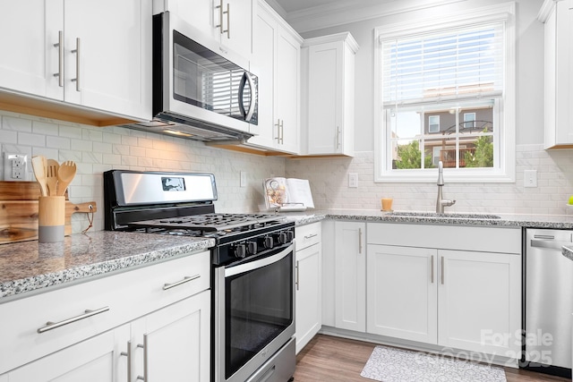 3038 Burnello Ct, Iron Station, NC 28080 - kitchen featuring appliances with stainless steel finishes, white cabinetry, ornamental molding, light stone countertops, and light wood-style floors