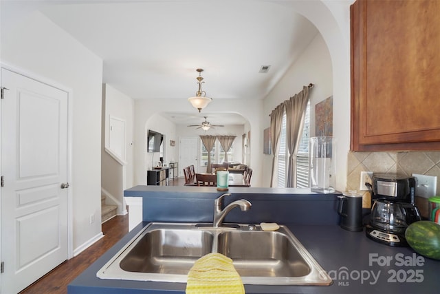 1012 Laparc Ln, Indian Trail, NC 28079 - kitchen with arched walkways, ceiling fan, decorative backsplash, dark wood finished floors, and brown cabinetry