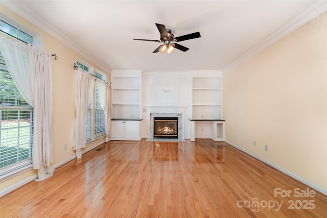1002 Hollyhedge Ln, Indian Trail, NC 28079 - unfurnished living room featuring light wood-style floors, a ceiling fan, a high end fireplace, crown molding, and built in shelves