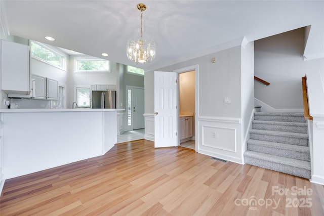 14053 Queens Harbor Rd, Charlotte, NC 28278 - unfurnished living room featuring a chandelier, stairway, light wood-style flooring, a decorative wall, and a wainscoted wall
