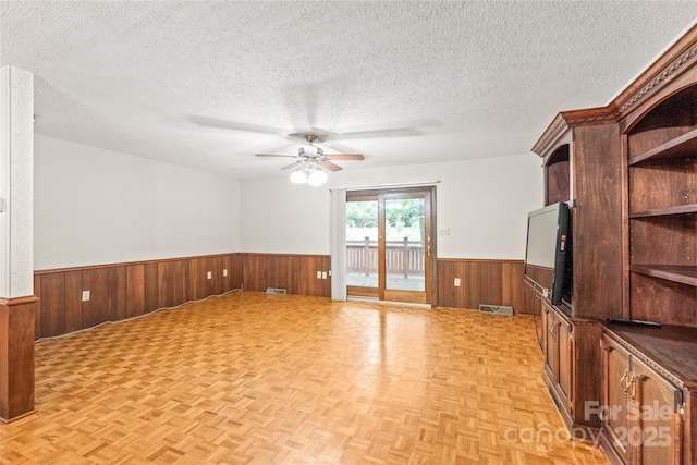 3985 Well Rd, Mint Hill, NC 28227 - unfurnished living room featuring wainscoting, a ceiling fan, wood walls, a textured ceiling, and parquet floors