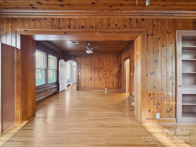 729 Montgomery Ave, Albemarle, NC 28001 - unfurnished living room with radiator, arched walkways, wood walls, light wood-type flooring, and a ceiling fan