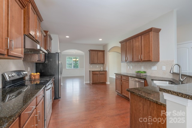 11922 Kimberfield Rd, Matthews, NC 28105 - kitchen with appliances with stainless steel finishes, under cabinet range hood, arched walkways, brown cabinets, and recessed lighting