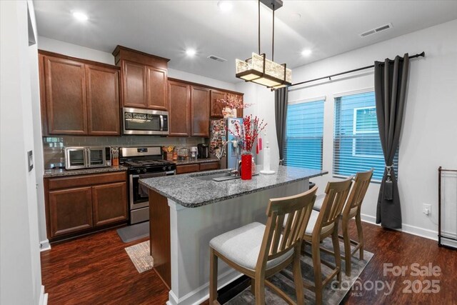 11965 Hambright Rd, Huntersville, NC 28078 - kitchen featuring appliances with stainless steel finishes, dark wood-type flooring, a kitchen island with sink, tasteful backsplash, and a breakfast bar area