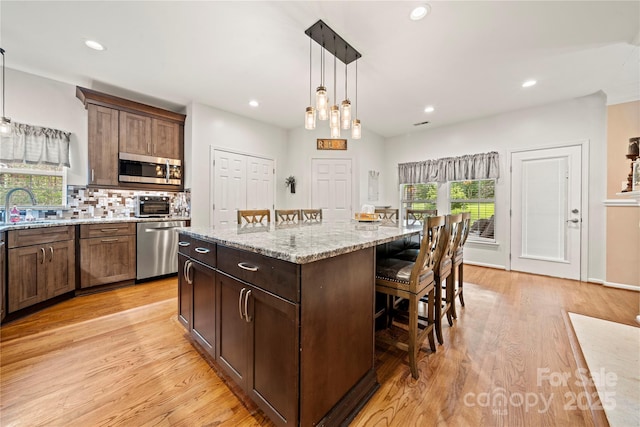 162 Castles Gate Dr, Mooresville, NC 28117 - kitchen featuring appliances with stainless steel finishes, a kitchen bar, a kitchen island, light wood finished floors, and tasteful backsplash