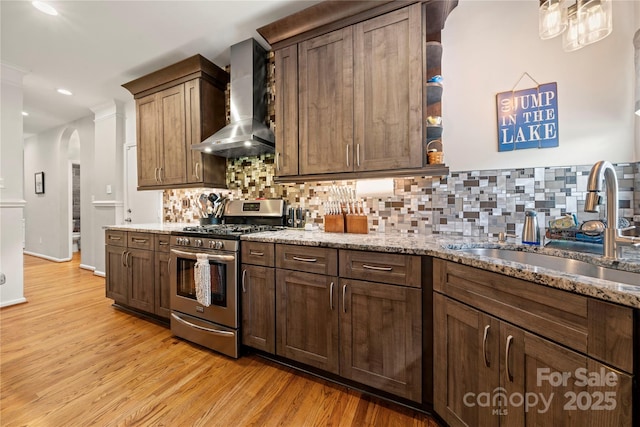 162 Castles Gate Dr, Mooresville, NC 28117 - kitchen with gas stove, wall chimney exhaust hood, light wood finished floors, arched walkways, and backsplash