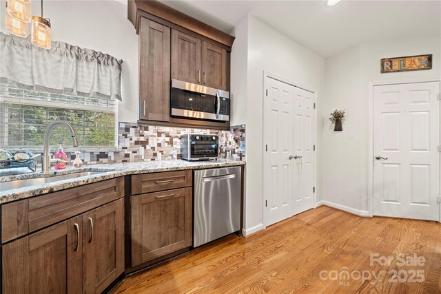 162 Castles Gate Dr, Mooresville, NC 28117 - kitchen featuring stainless steel appliances, tasteful backsplash, light wood-type flooring, light stone countertops, and decorative light fixtures