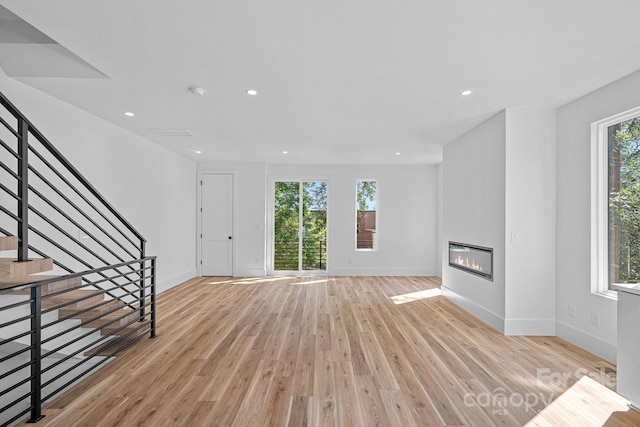 209 Keswick Ave, Charlotte, NC 28206 - unfurnished living room with light wood-type flooring, a glass covered fireplace, recessed lighting, and stairs