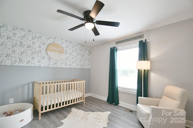 339 Brown Rd, China Grove, NC 28023 - bedroom featuring a crib, a wainscoted wall, wood finished floors, and a ceiling fan