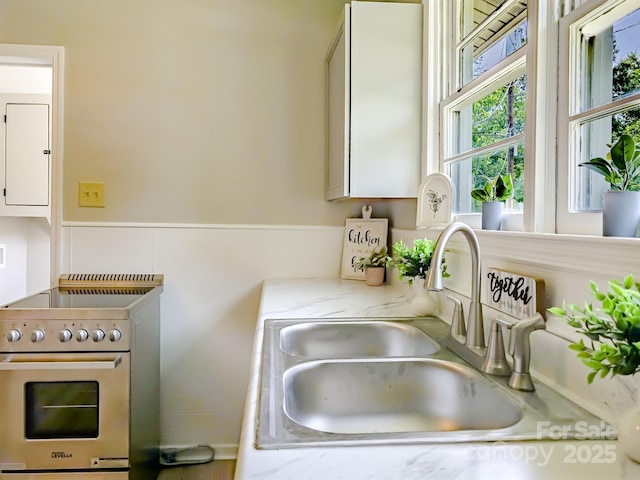 106 Cedar St, Spindale, NC 28160 - kitchen featuring stainless steel electric stove, a sink, light stone countertops, and a wainscoted wall
