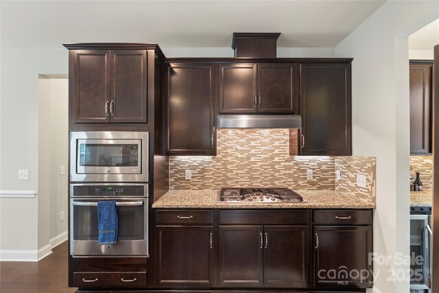 1830 Alden Oaks Ln, Charlotte, NC 28270 - kitchen with appliances with stainless steel finishes, under cabinet range hood, light stone countertops, tasteful backsplash, and dark brown cabinets