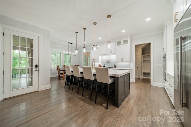 2004 Viscount Dr, Matthews, NC 28104 - kitchen featuring a large island with sink, white cabinetry, wood finished floors, a kitchen bar, and glass insert cabinets