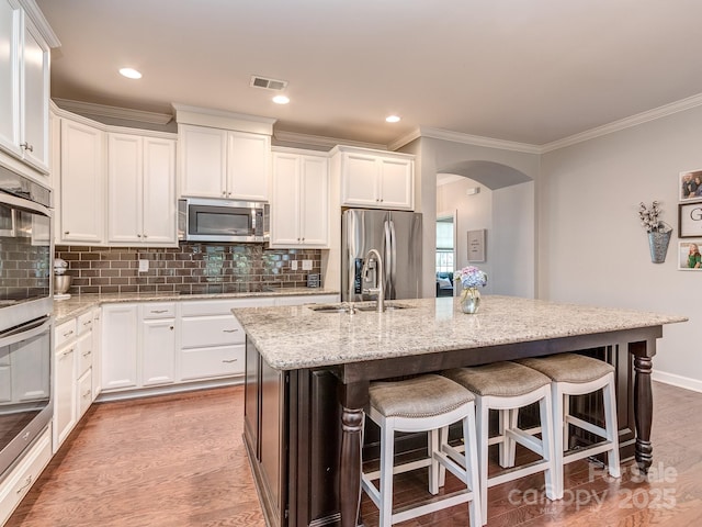 314 Candella Dr, Matthews, NC 28104 - kitchen featuring stainless steel appliances, a sink, crown molding, arched walkways, and an island with sink