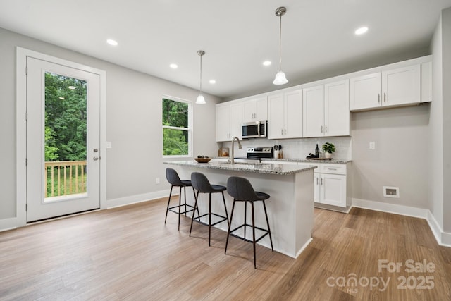 384 Speedway Pl, Concord, NC 28027 - kitchen with appliances with stainless steel finishes, decorative backsplash, white cabinets, light stone counters, and light wood-style flooring