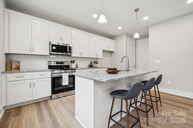 384 Speedway Pl, Concord, NC 28027 - kitchen featuring stainless steel appliances, white cabinets, tasteful backsplash, light wood-style floors, and a breakfast bar area