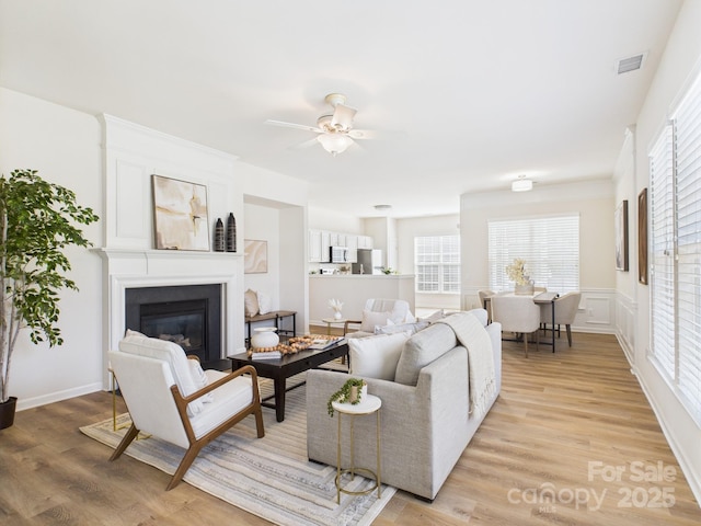9030 Gander Dr, Charlotte, NC 28277 - living area with a glass covered fireplace, light wood-type flooring, ceiling fan, healthy amount of natural light, and a wainscoted wall