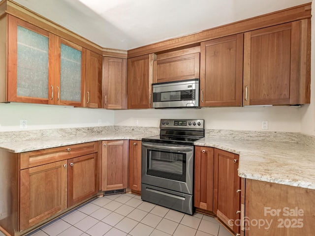 3310 Windbluff Dr, Charlotte, NC 28277 - kitchen with appliances with stainless steel finishes, light tile patterned floors, brown cabinets, glass insert cabinets, and light stone counters