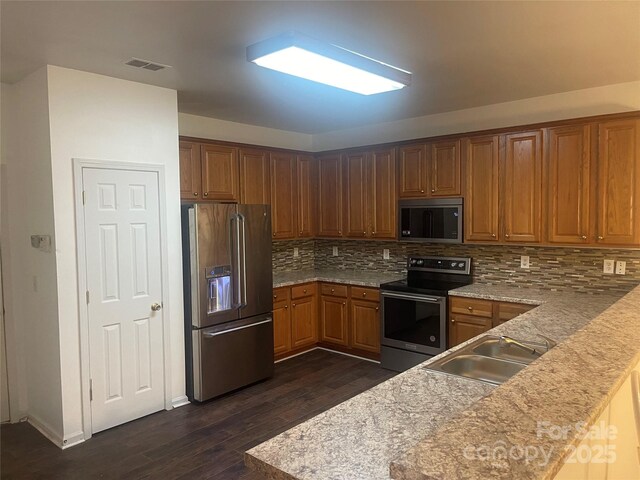 4454 Glenlea Commons Dr, Charlotte, NC 28216 - kitchen with appliances with stainless steel finishes, dark wood-style flooring, backsplash, brown cabinetry, and a peninsula