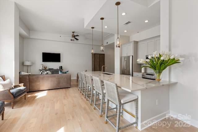 1315 E Blvd Unit 225, Charlotte, NC 28203 - kitchen with appliances with stainless steel finishes, light stone countertops, ceiling fan, a breakfast bar area, and light wood-style flooring
