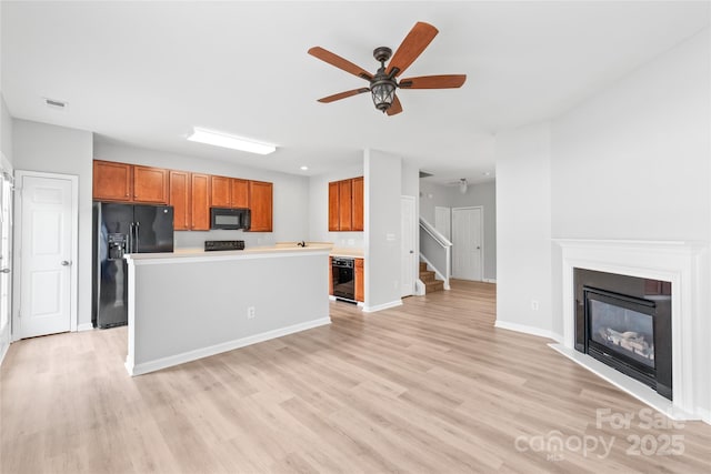 12452 Stratfield Place Cir, Pineville, NC 28134 - kitchen with black appliances, brown cabinetry, a ceiling fan, light wood-style floors, and a glass covered fireplace