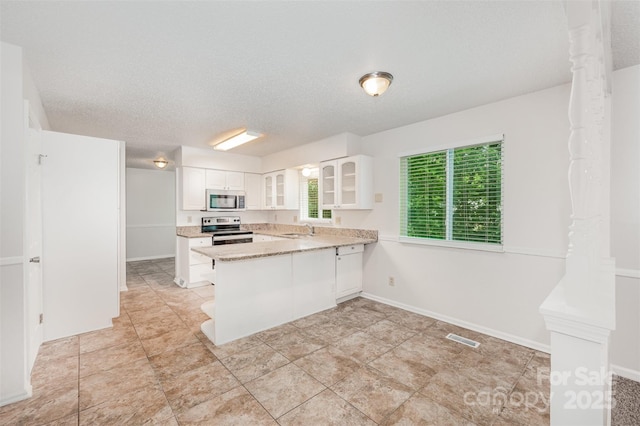 7008 Wannamaker Ln, Charlotte, NC 28226 - kitchen with appliances with stainless steel finishes, a peninsula, glass insert cabinets, white cabinets, and a textured ceiling