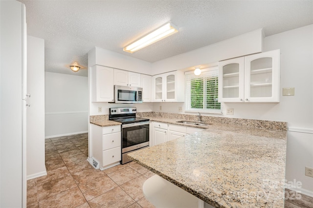 7008 Wannamaker Ln, Charlotte, NC 28226 - kitchen featuring stainless steel appliances, glass insert cabinets, a peninsula, white cabinetry, and a textured ceiling