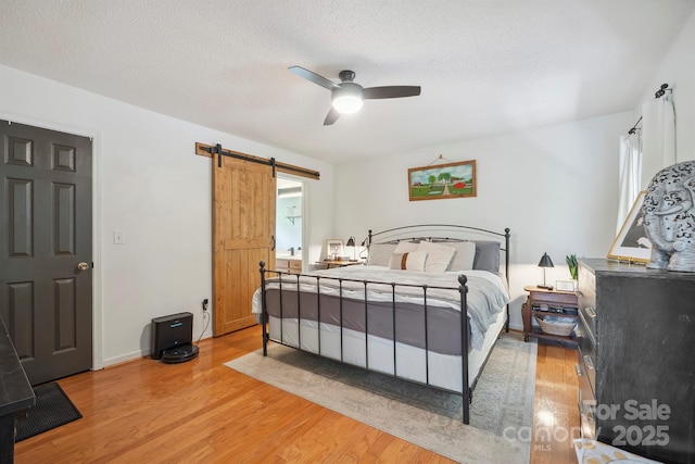 3381 Stones Throw Dr, Valdese, NC 28690 - bedroom featuring a barn door, light wood-type flooring, ceiling fan, and a textured ceiling
