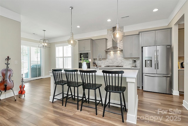 5129 Whitman Ave, Matthews, NC 28105 - kitchen featuring appliances with stainless steel finishes, gray cabinetry, light countertops, wall chimney exhaust hood, and a kitchen breakfast bar
