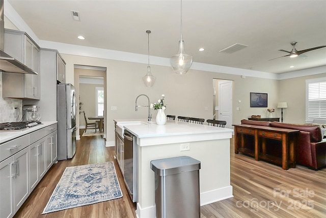 5129 Whitman Ave, Matthews, NC 28105 - kitchen with wall chimney exhaust hood, gray cabinets, stainless steel appliances, a center island with sink, and light countertops