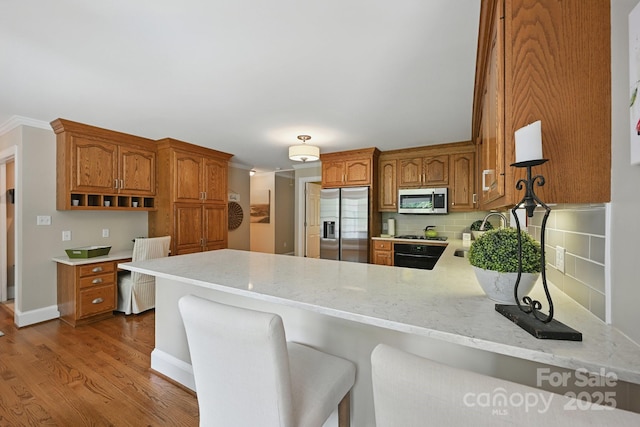 4824 Waxhaw Farms Rd, Waxhaw, NC 28173 - kitchen with appliances with stainless steel finishes, a peninsula, tasteful backsplash, brown cabinetry, and wood finished floors