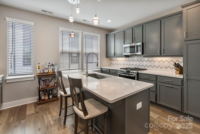 2969 Simpson Dr, Charlotte, NC 28205 - kitchen featuring appliances with stainless steel finishes, tasteful backsplash, wood finished floors, a kitchen bar, and hanging light fixtures