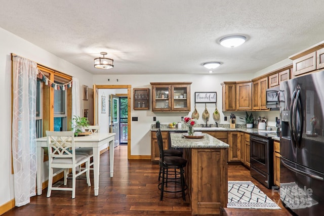 2171 Black Rock Rd, Cherokee, NC 28719 - kitchen with stainless steel appliances, brown cabinetry, a breakfast bar area, a textured ceiling, and dark wood finished floors