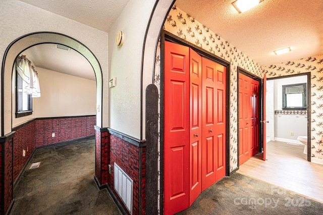 4275 Herman Sipe Rd, Conover, NC 28613 - hallway featuring a textured ceiling, wallpapered walls, carpet, arched walkways, and wainscoting