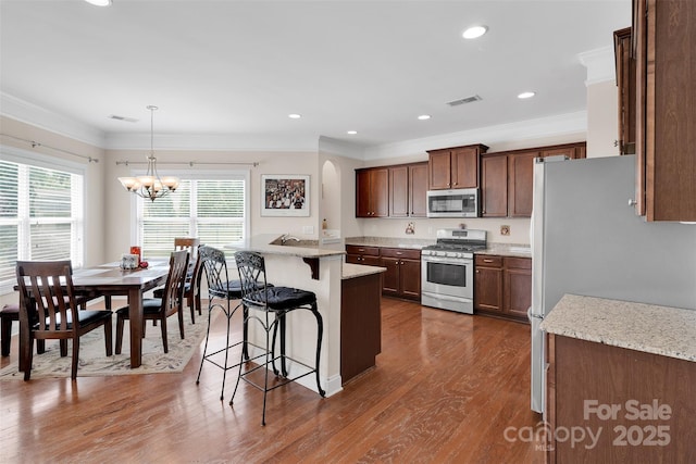 1636 Ridge Haven Rd, Waxhaw, NC 28173 - kitchen with stainless steel appliances, a kitchen bar, ornamental molding, a chandelier, and dark wood finished floors