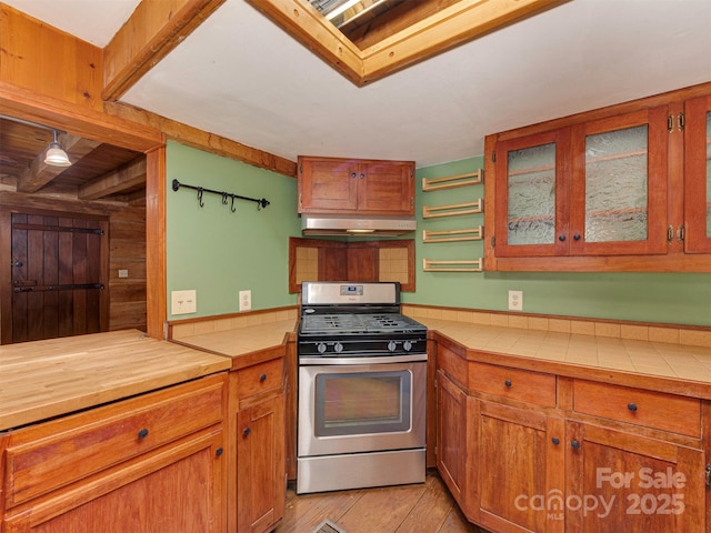 5109 Walnut Grove Ln, Charlotte, NC 28227 - kitchen featuring stainless steel range with gas cooktop, under cabinet range hood, tile countertops, light wood-style floors, and brown cabinetry