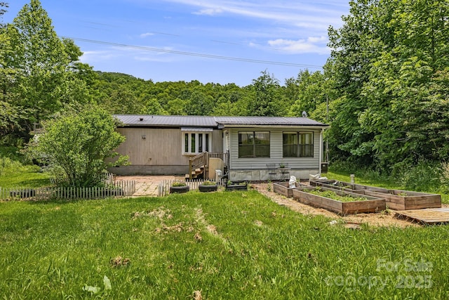 311 Flynn Br, Madison, NC 28753 - rear view of house featuring a vegetable garden, a metal roof, a yard, and a wooded view