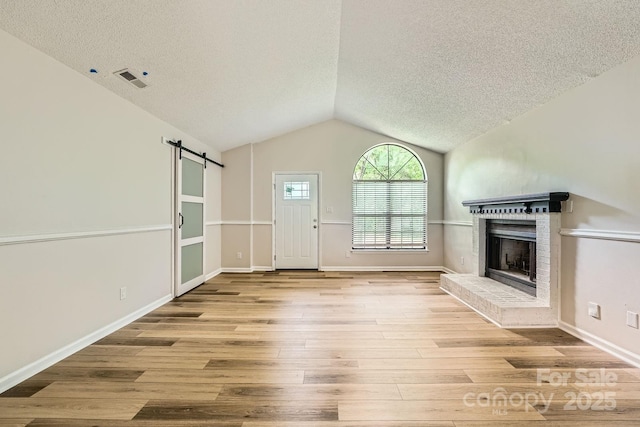 5817 Rocky Mount Ct, Charlotte, NC 28214 - unfurnished living room with a textured ceiling, a barn door, a fireplace, wood finished floors, and vaulted ceiling