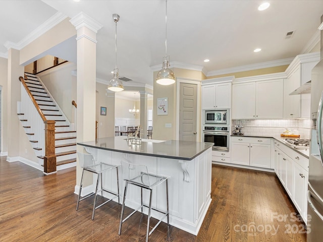 612 Ideal Way, Charlotte, NC 28203 - kitchen featuring appliances with stainless steel finishes, ornate columns, dark countertops, a breakfast bar area, and dark wood-style flooring