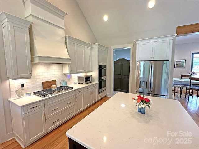 4282 Brandy Creek Ct, Clover, SC 29710 - kitchen with stainless steel appliances, decorative backsplash, light wood-type flooring, lofted ceiling, and custom range hood