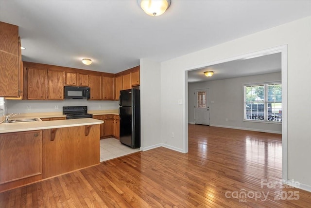 1011 Atherstone St NW, Conover, NC 28613 - kitchen with black appliances, light countertops, a peninsula, light wood-type flooring, and brown cabinetry