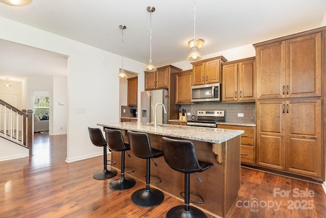 1691 Ashley Lynn Ct, Stanfield, NC 28163 - kitchen with appliances with stainless steel finishes, brown cabinetry, dark wood finished floors, decorative backsplash, and an island with sink