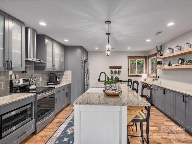 505 Scenic Cir, Waynesville, NC 28786 - kitchen featuring stainless steel appliances, wall chimney range hood, a kitchen bar, gray cabinetry, and light wood-style floors