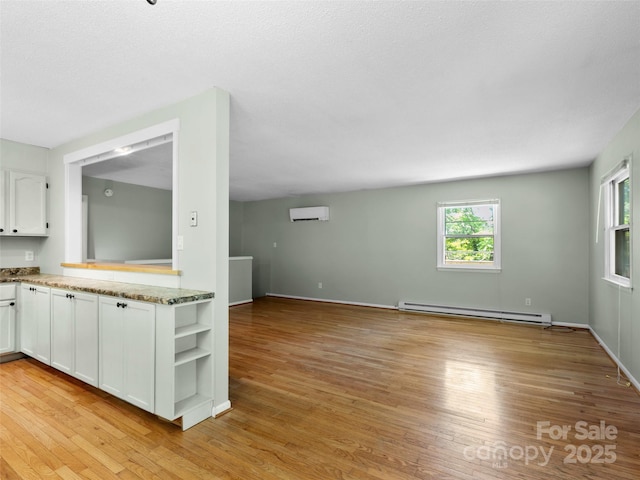 45 Avondale Heights Rd, Asheville, NC 28803 - kitchen with a baseboard heating unit, an AC wall unit, white cabinetry, and light wood-type flooring