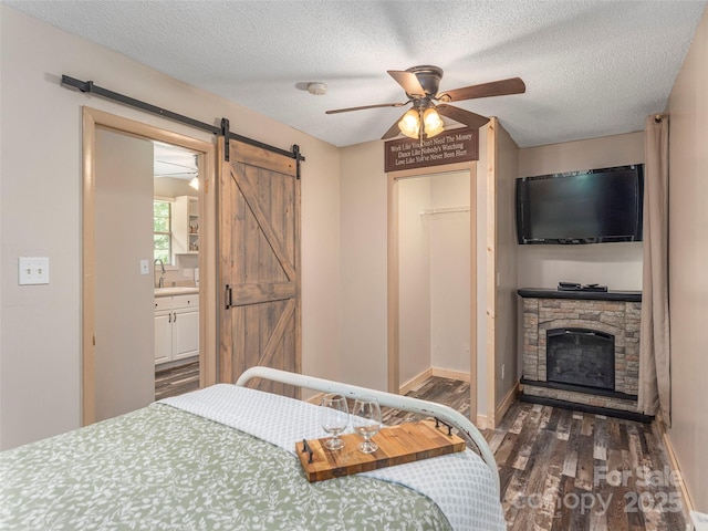 1131 Laurel Branch Rd, Waynesville, NC 28785 - bedroom with a barn door, wood finished floors, a stone fireplace, a textured ceiling, and ensuite bathroom