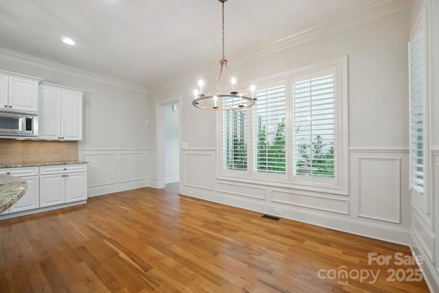 20635 Queensdale Dr, Cornelius, NC 28031 - unfurnished dining area with a decorative wall, a chandelier, light wood-style floors, ornamental molding, and wainscoting