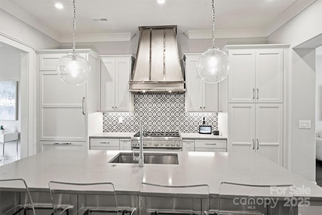 622 Mattie Rose Ln, Charlotte, NC 28204 - kitchen with custom range hood, a large island with sink, stainless steel range with gas cooktop, white cabinets, and decorative light fixtures